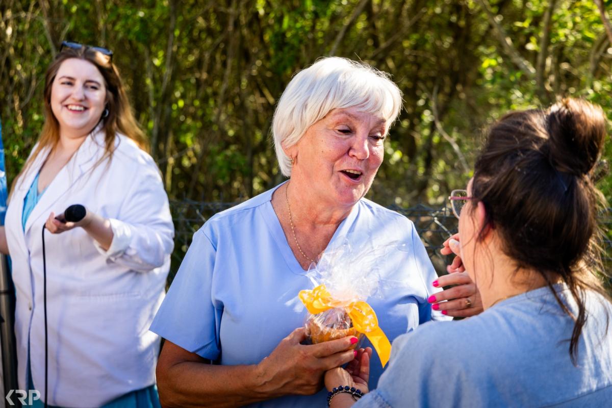 Mitarbeiterin von JaSo24 überreicht einer Seniorin lachend ein kleines Geschenk