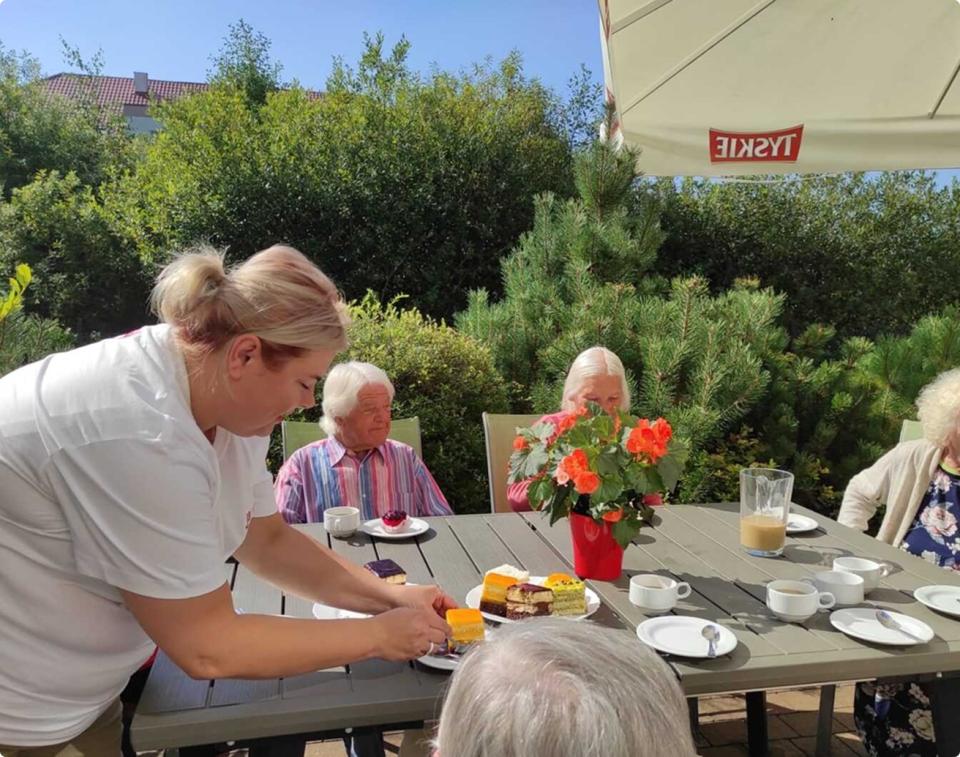 Betreuerin serviert Seniorinnen und Senioren Kuchen an einem Gartentisch – Seniorenbetreuung in Idar-Oberstein