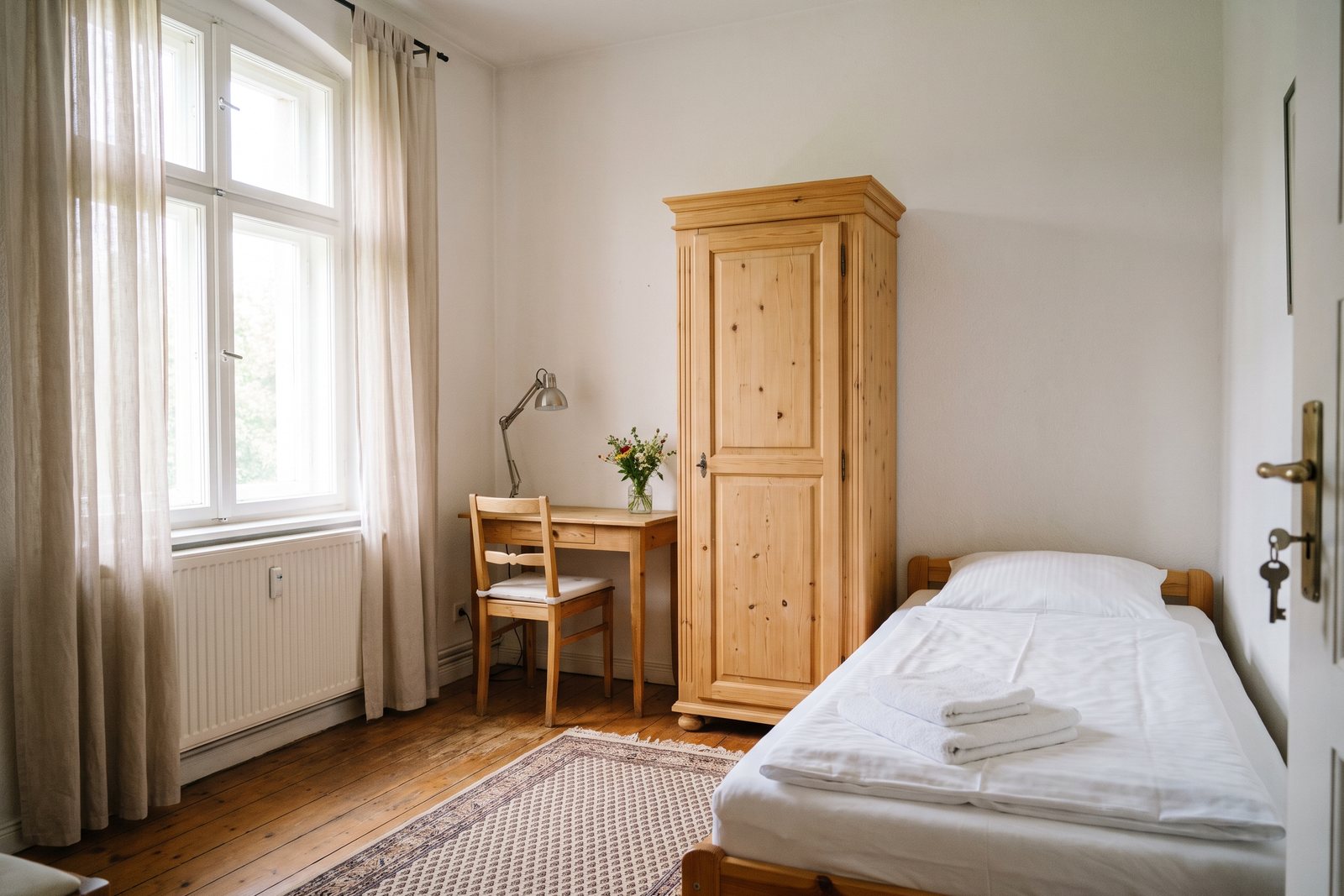 Vorbereitetes Zimmer für die Betreuungskraft mit Bett, Schrank, Schreibtisch und Fenster